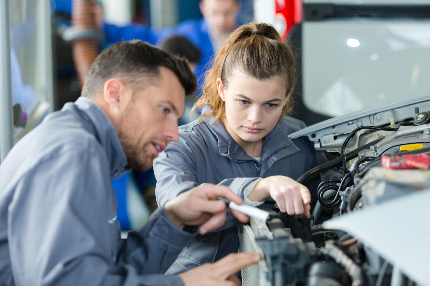 Ein Berufsbildner zeigt einem Lehrling, wie er den Automotor untersuchen muss.